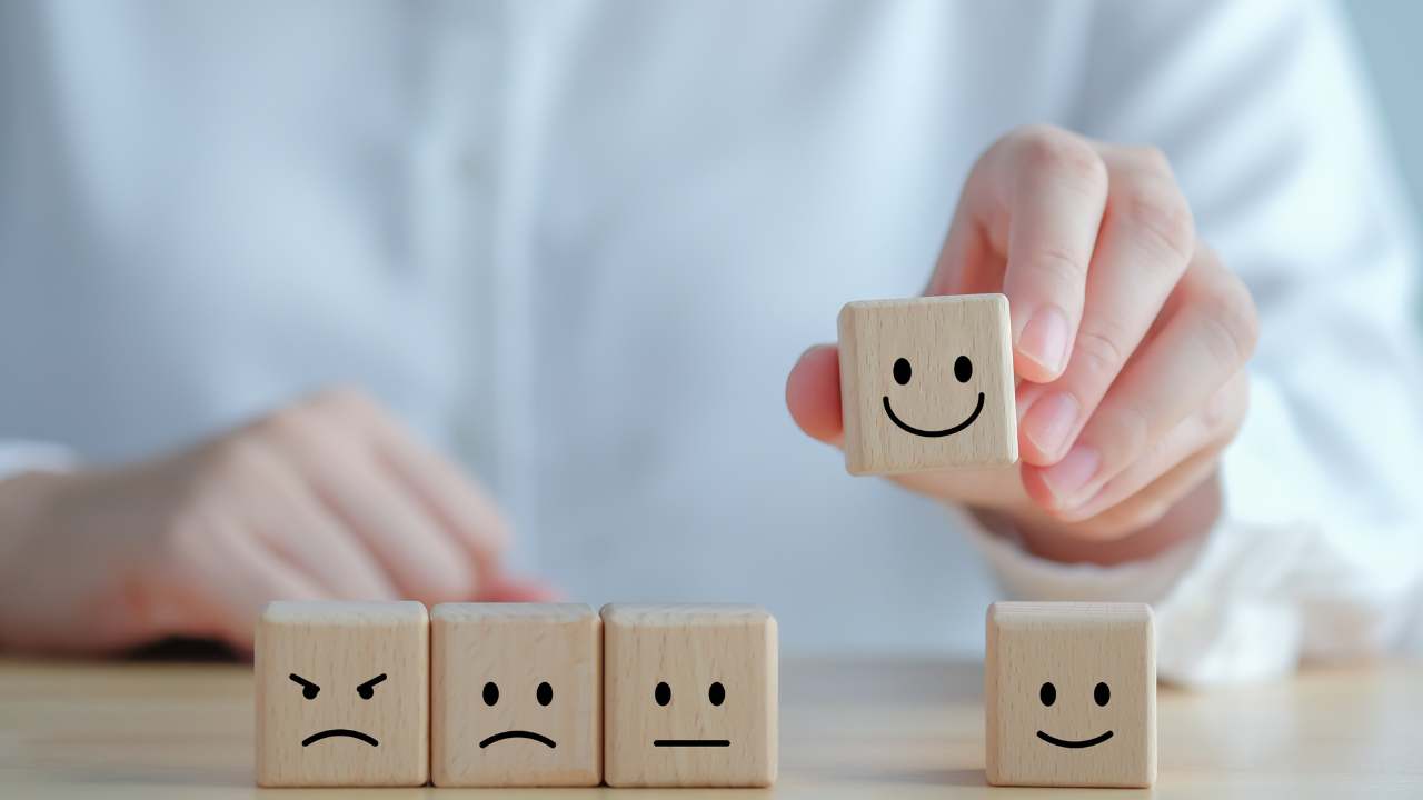 Hand placing a smiling wooden block above a row of blocks showing angry, sad, neutral, and happy faces