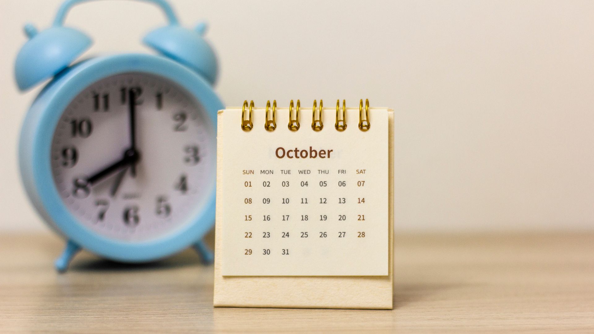 Small October desk calendar beside a light blue alarm clock on a wooden table