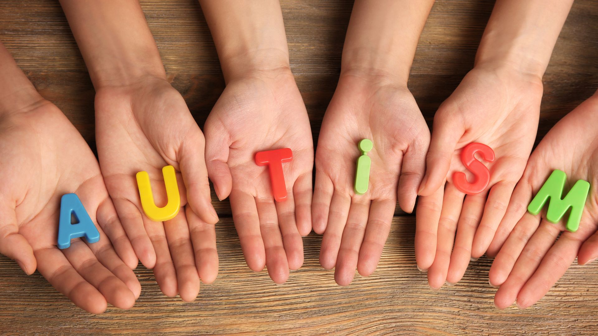 Open hands holding colorful letters spelling AUTISM on a wooden surface