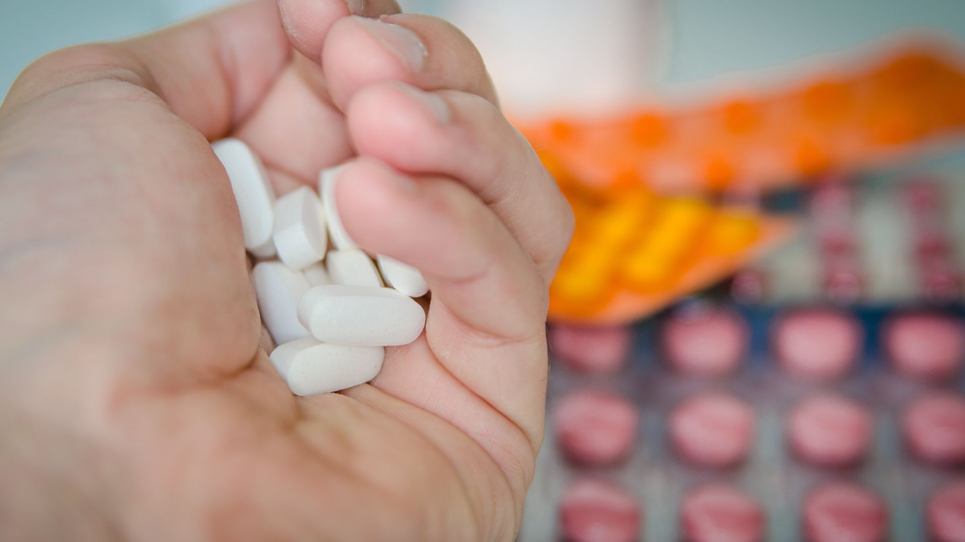 Open hand holding several white medication tablets with blister packs in the background